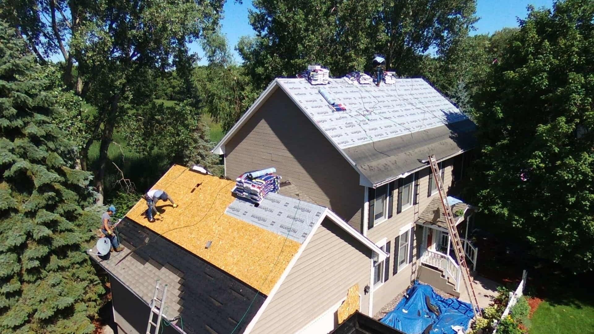 Roofers working on a multi-level house with ladders and shingles